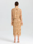 A woman faces away, wearing the Social Queen Beaded Fringe Slit Midi Skirt in a nude floral embroidery with beaded fringe. Her midi skirt features mesh accents, paired with heeled sandals and a braided updo.