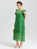 A woman wears the Social Queen Floral Silk Velvet Shift Dress (Cami Included)—a loose, green velvet style with delicate floral motifs—holding a small handbag and standing against a plain light background.