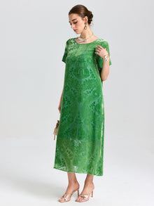 A woman wears the Social Queen Floral Silk Velvet Shift Dress (Cami Included)—a loose, green velvet style with delicate floral motifs—holding a small handbag and standing against a plain light background.