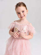 A young girl smiles against a plain, light background wearing the Social Queen Girls Floral Sequin Tulle Dress in light pink with ruffled details.