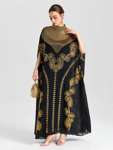 A woman wears Social Queen's Beaded Embroidered Cape Dress—black and gold chiffon with Persian-inspired details—styled with a matching handbag and strappy heels against a plain light background, ideal for evening occasions.