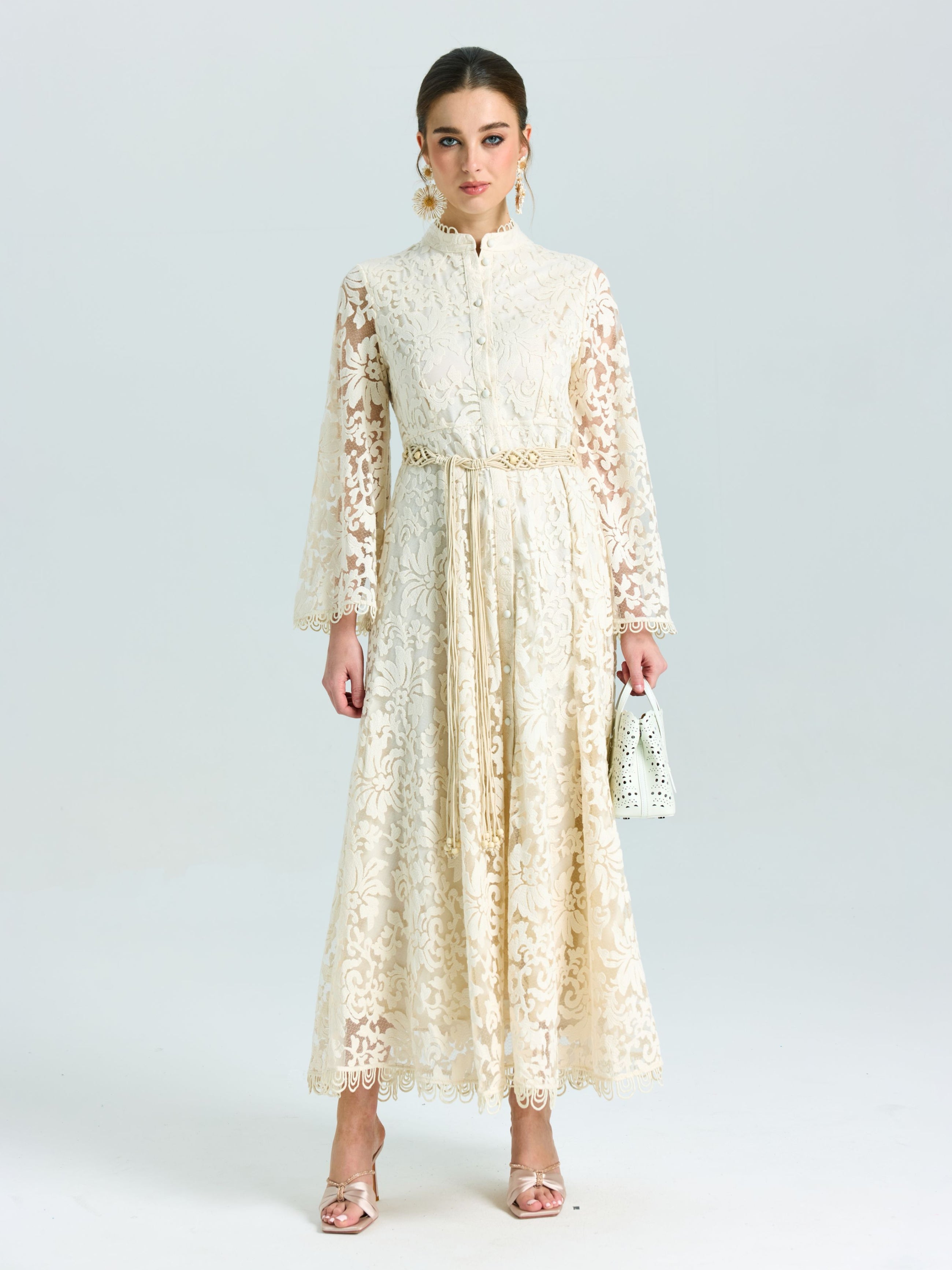 A woman wears the Social Queen Embroidered Lace High-Neck Dress, featuring long sleeves and baroque floral embroidery, paired with a white handbag against a plain light background.