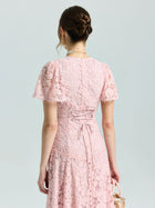 A woman, seen from behind with her hair in a low bun, holds a small purse while wearing the Social Queen Floral Embroidered Lace Dress with short sleeves.