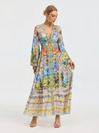 A woman models the Social Queen Garden Print Silk Maxi Dress, featuring a deep V-neck, long sleeves, and a fitted waist, against a plain white background.