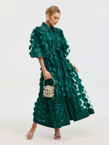 A woman wears the Social Queen Pearl Embellished Appliqué Dress, featuring green textured fabric with large polka dots and crystal pearl details. She pairs it with a small purse and silver strappy heels against a plain background.