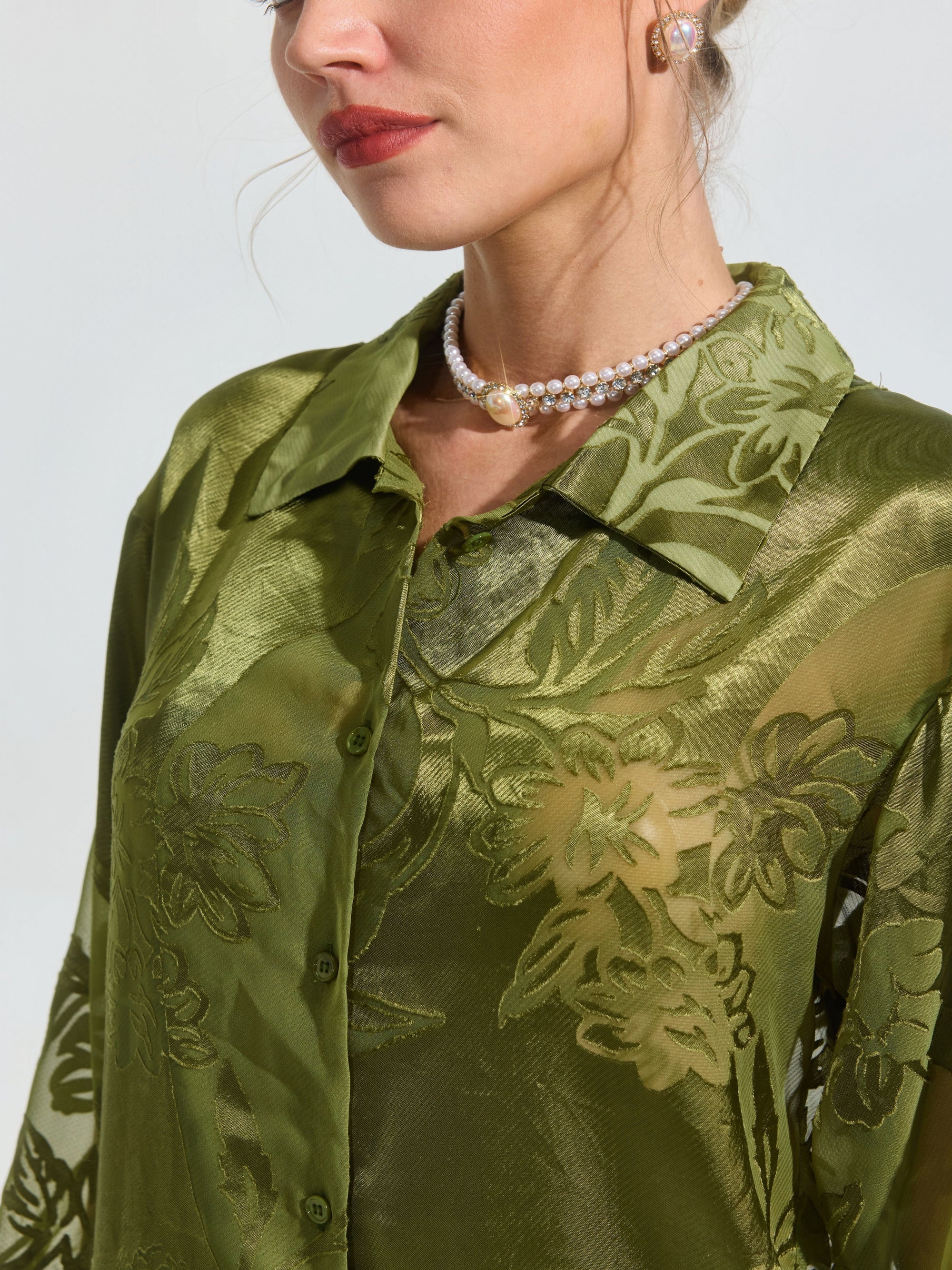 Close-up of a woman wearing the Social Queen Beaded Botanical Burnout Satin Shirt in olive green, styled with a pearl necklace, light pink lipstick, and small earrings.