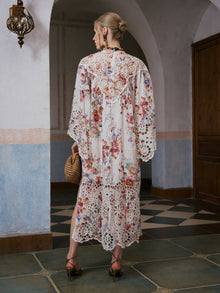 A woman stands indoors on a tiled floor, facing away from the camera, wearing the Social Queen Floral Print Cutwork Linen Dress and heels, and carrying a woven handbag.