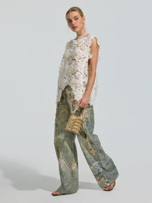 A woman wearing the Social Queen Pearl Rose Guipure Lace Top, wide-leg printed jeans, and sandals, holding a small straw handbag, stands against a plain light background.