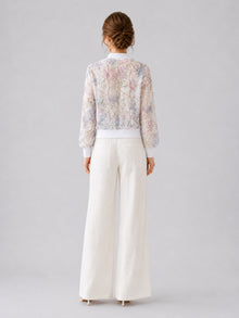 A woman stands with her back to the camera against a plain light gray background, wearing Social Queen’s Casual Wide-Leg Pants with a textured finish and a sheer, patterned blouse.