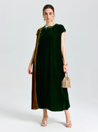 A woman wears the Social Queen Colorblock Silk Velvet Shift Dress with gold drape detail, paired with a small woven handbag and open-toe heels, against a plain light background.
