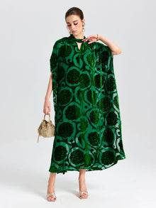A woman in a loose, green Floral Velvet Cape Dress (Cami Included) by Social Queen holds a small handbag while standing against a plain white background.