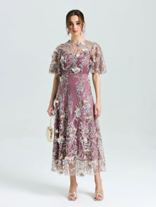A woman faces forward, wearing the Social Queen Floral Beaded A-Line Dress with flutter sleeves, holding a small beige purse, and open-toe heels.