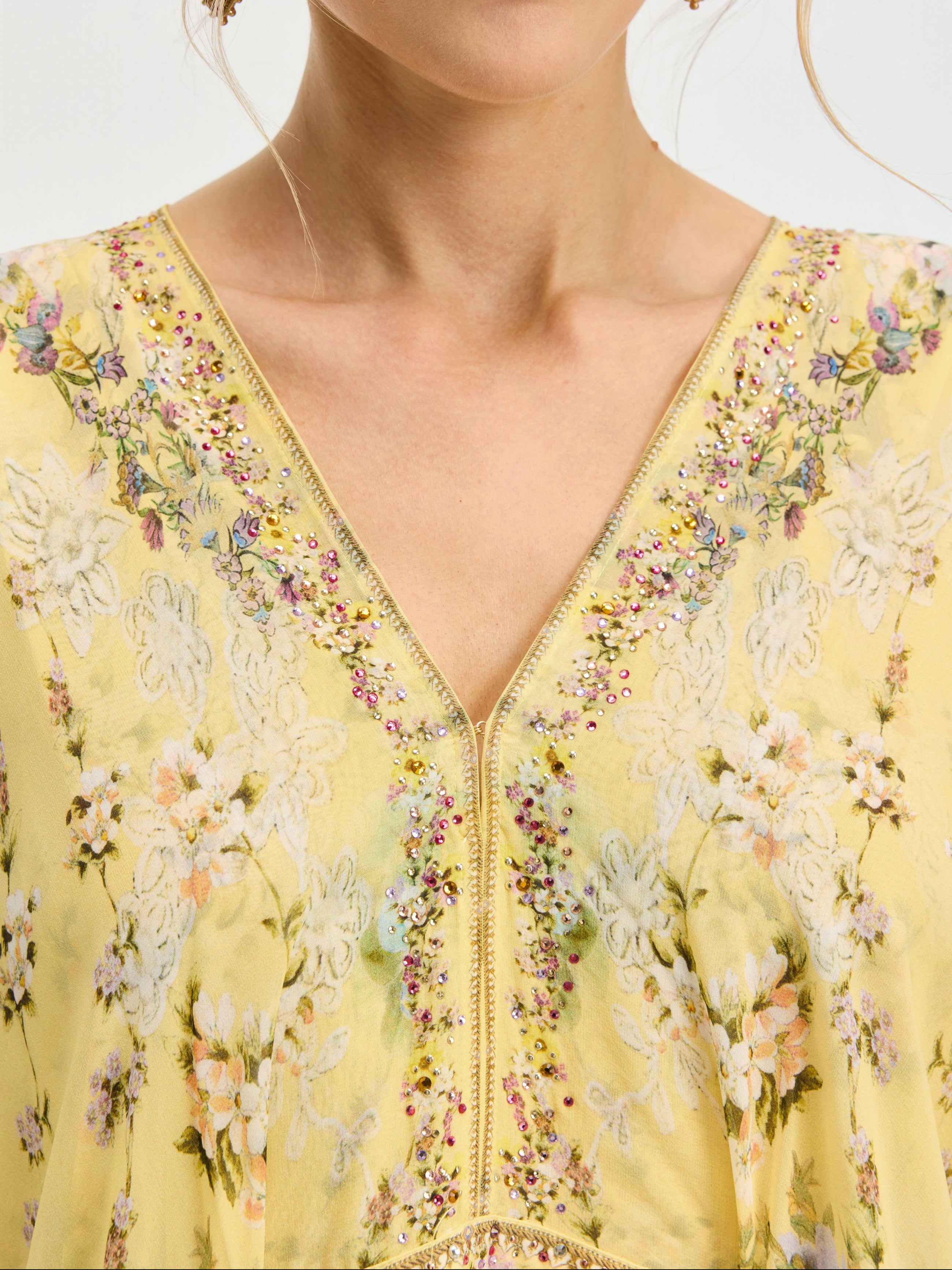 A close-up of a person wearing the Social Queen Floral Print Silk Caftan Dress, featuring a yellow floral pattern, deep V-neckline, sequins, and embroidered flowers—an elegant choice for resort wear.