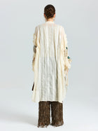A person faces away wearing Social Queen's Floral Embroidered Linen Jacket with cami, featuring textured cream linen and subtle floral embroidery, paired with wide dark fringed pants against a plain white background.