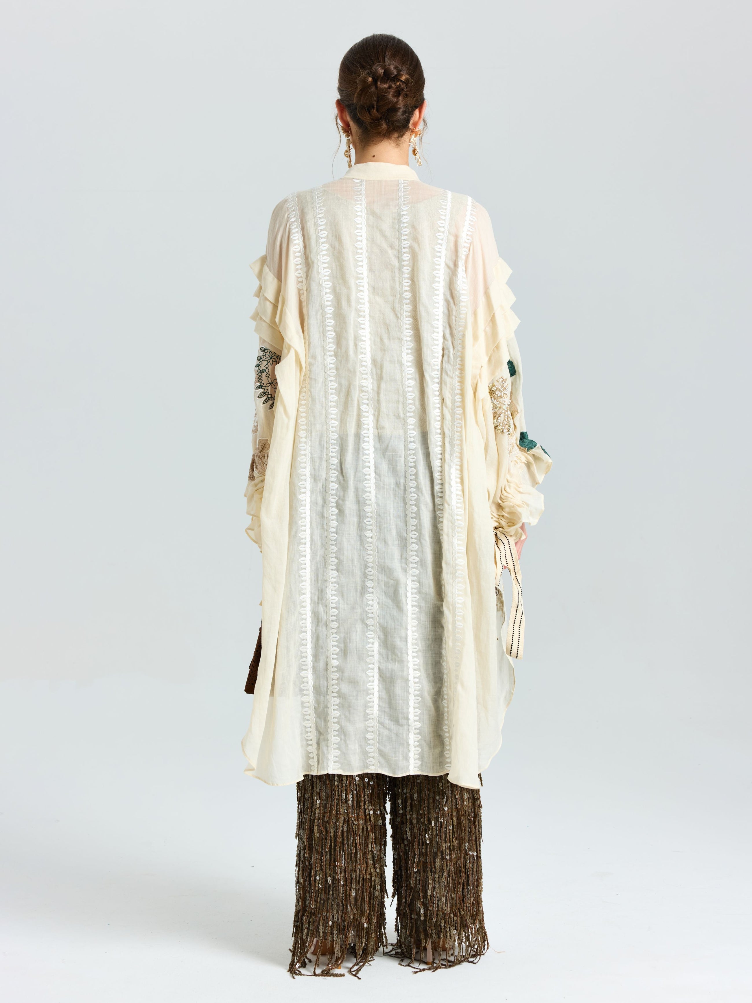A person faces away wearing Social Queen's Floral Embroidered Linen Jacket with cami, featuring textured cream linen and subtle floral embroidery, paired with wide dark fringed pants against a plain white background.