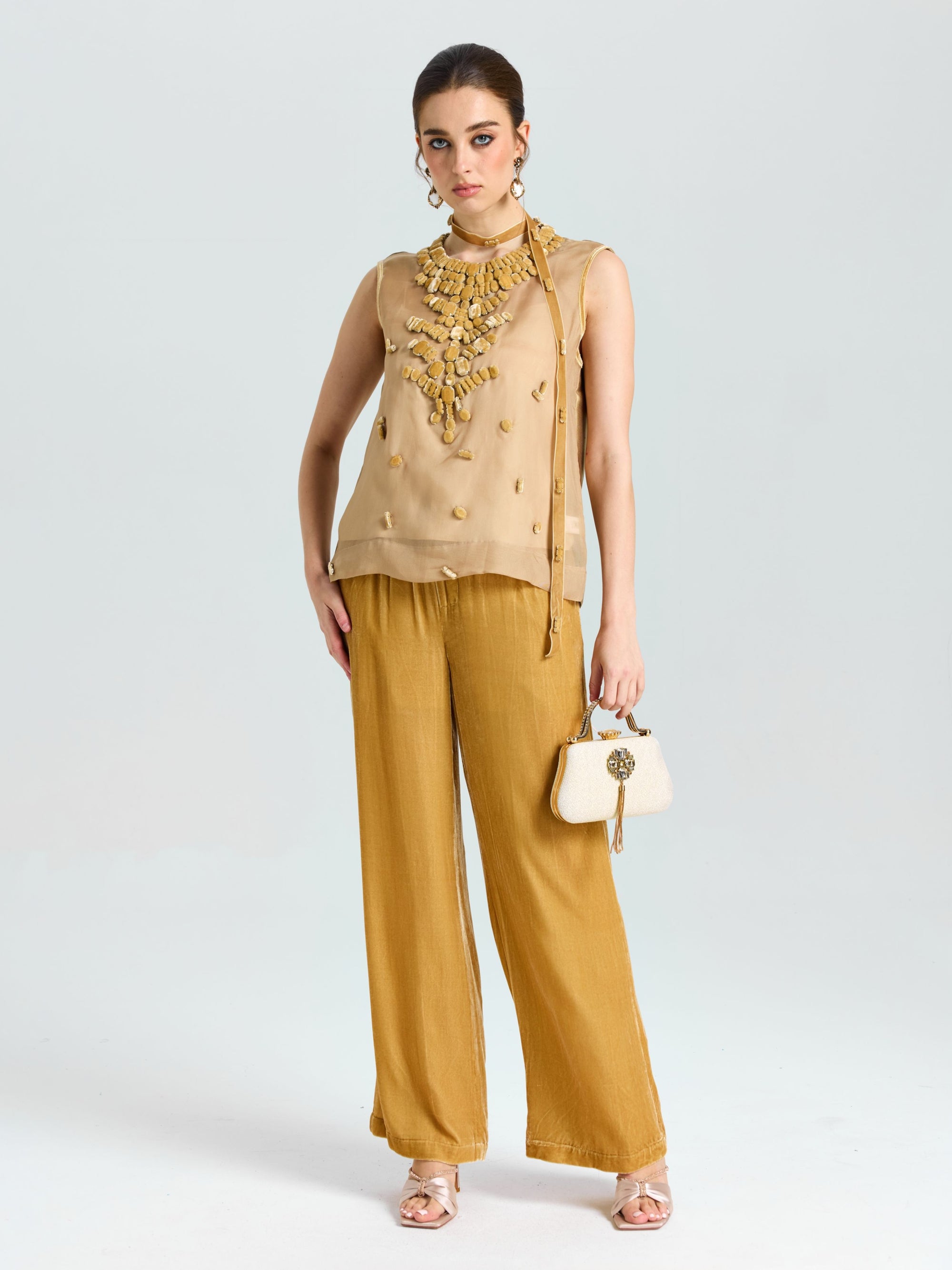 A woman stands against a plain light background in the Social Queen Velvet Scarf Silk Organza Top (cami included), paired with wide-leg mustard pants, heels, and holding a small white handbag.