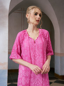 A woman with blonde hair in a low bun wears the Social Queen Geometric Jacquard Mulberry Silk Dress in bright pink, standing indoors near an arched doorway with neutral-toned walls and geometric floor tiles.