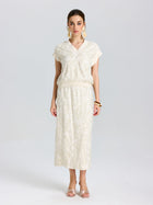 A woman stands facing forward, wearing the Social Queen Floral Embroidered Linen Top and a matching midi skirt, paired with beige heels, large earrings, and a brown bangle.