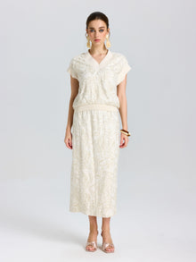 A woman stands facing forward, wearing the Social Queen Floral Embroidered Linen Top and a matching midi skirt, paired with beige heels, large earrings, and a brown bangle.