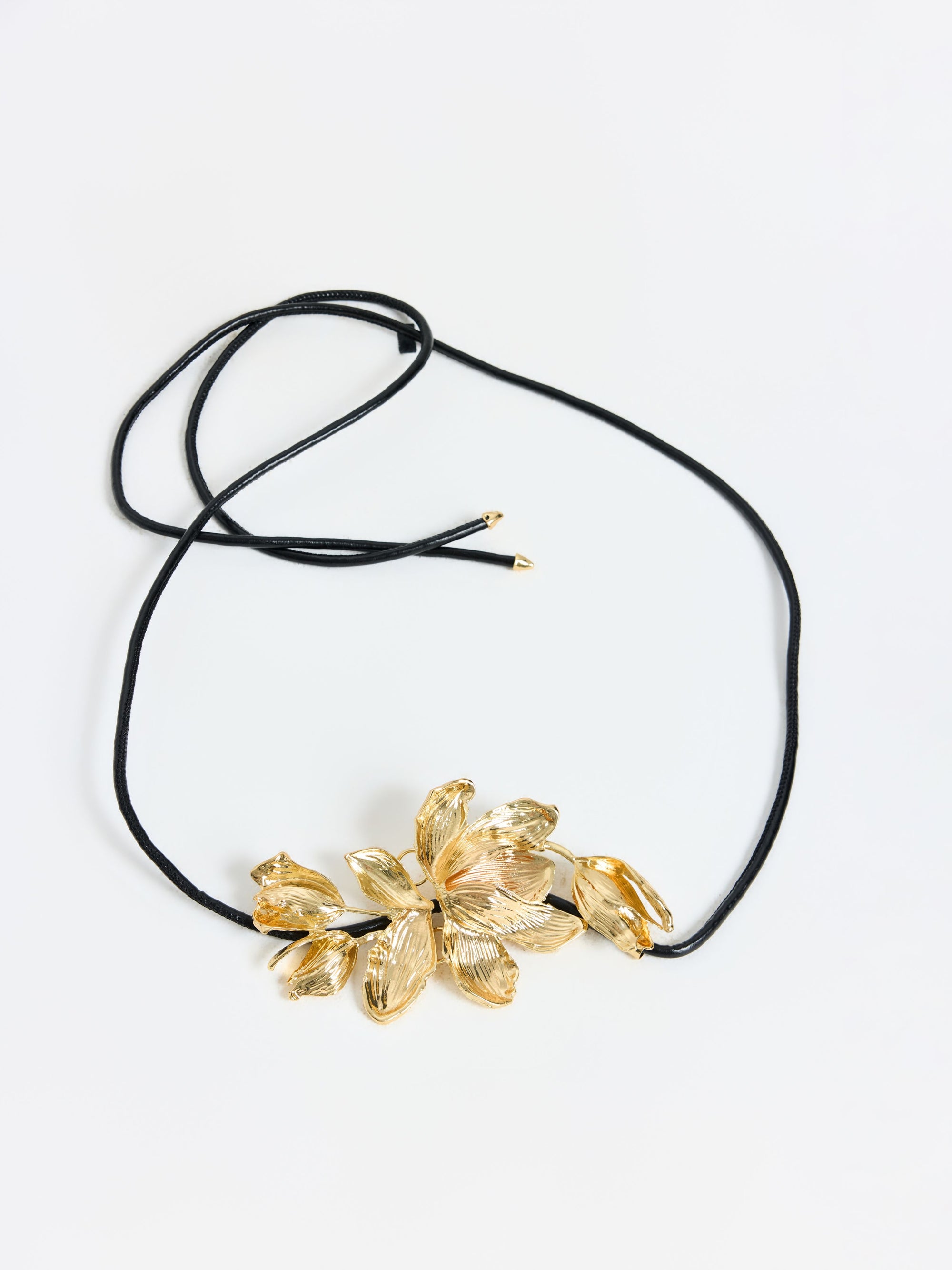The Social Queen Gilded Magnolia Petal Belt features a bold gold flower design on a black adjustable belt, beautifully showcased against a white backdrop.