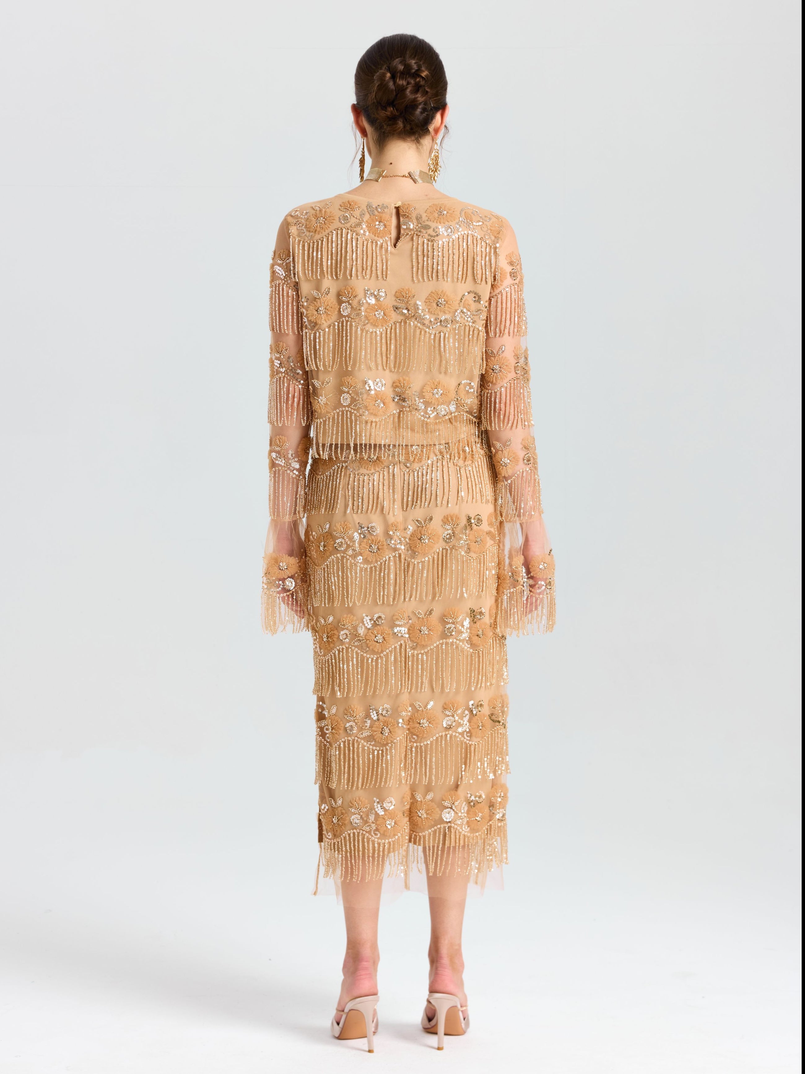 A woman faces away, wearing the Social Queen Beaded Fringe Floral Top paired with white heeled sandals, set against a plain background.