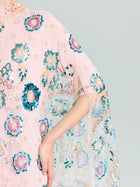 A person wears the Beaded Floral Embellished Cape Gown by Social Queen, featuring pink fabric with blue, green, and white floral sequins; their arm is bent at the elbow.