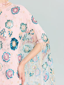A person wears the Beaded Floral Embellished Cape Gown by Social Queen, featuring pink fabric with blue, green, and white floral sequins; their arm is bent at the elbow.