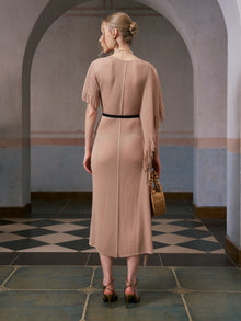 A woman stands with her back to the camera in a tiled, arched hallway, wearing the Social Queen Asymmetric Fringe Midi Dress (belt included) and heeled sandals, while holding a woven bag.