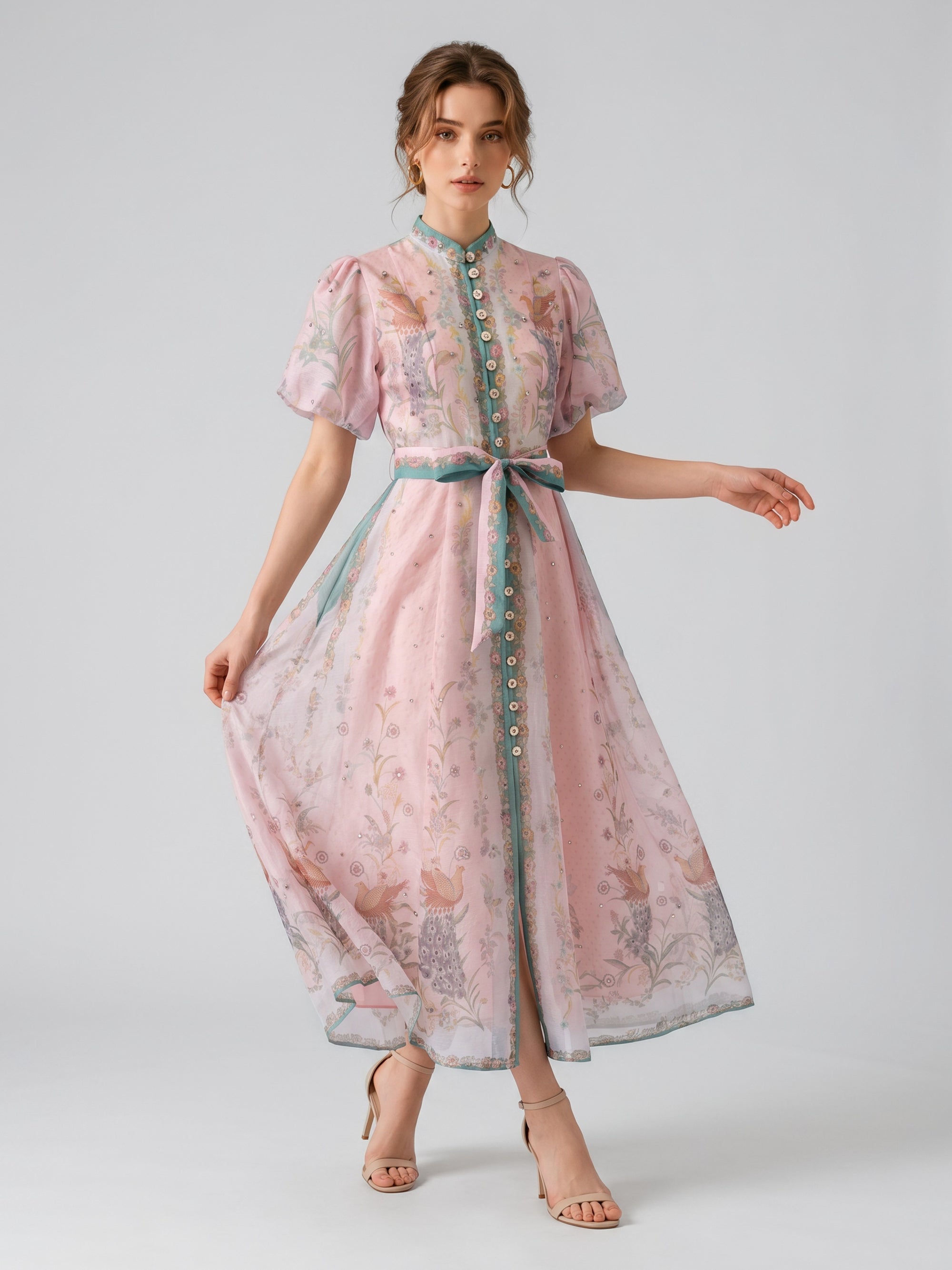 A woman wearing the Social Queen Peacock Botanical Print Dress, an ankle-length, light pink dress with a floral pattern, short sleeves, and a belted waist that creates an elegant A-line silhouette, stands against a plain background.