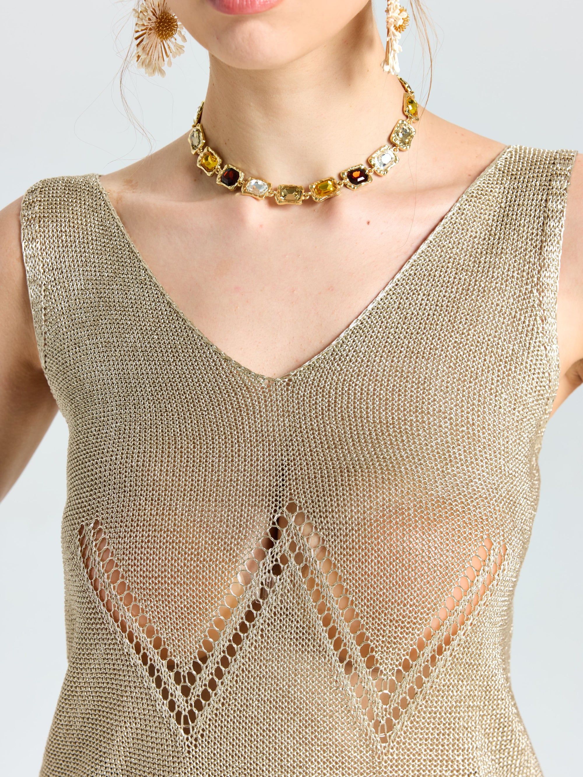 A woman wears the Social Queen Open-Knit Metallic Sleeveless Top with zigzag cutouts and a gemstone choker; her face is partially visible.