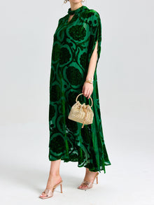 A person wears the Social Queen Floral Velvet Cape Dress (Cami Included), paired with a small woven handbag and open-toe heeled sandals, standing against a plain background.