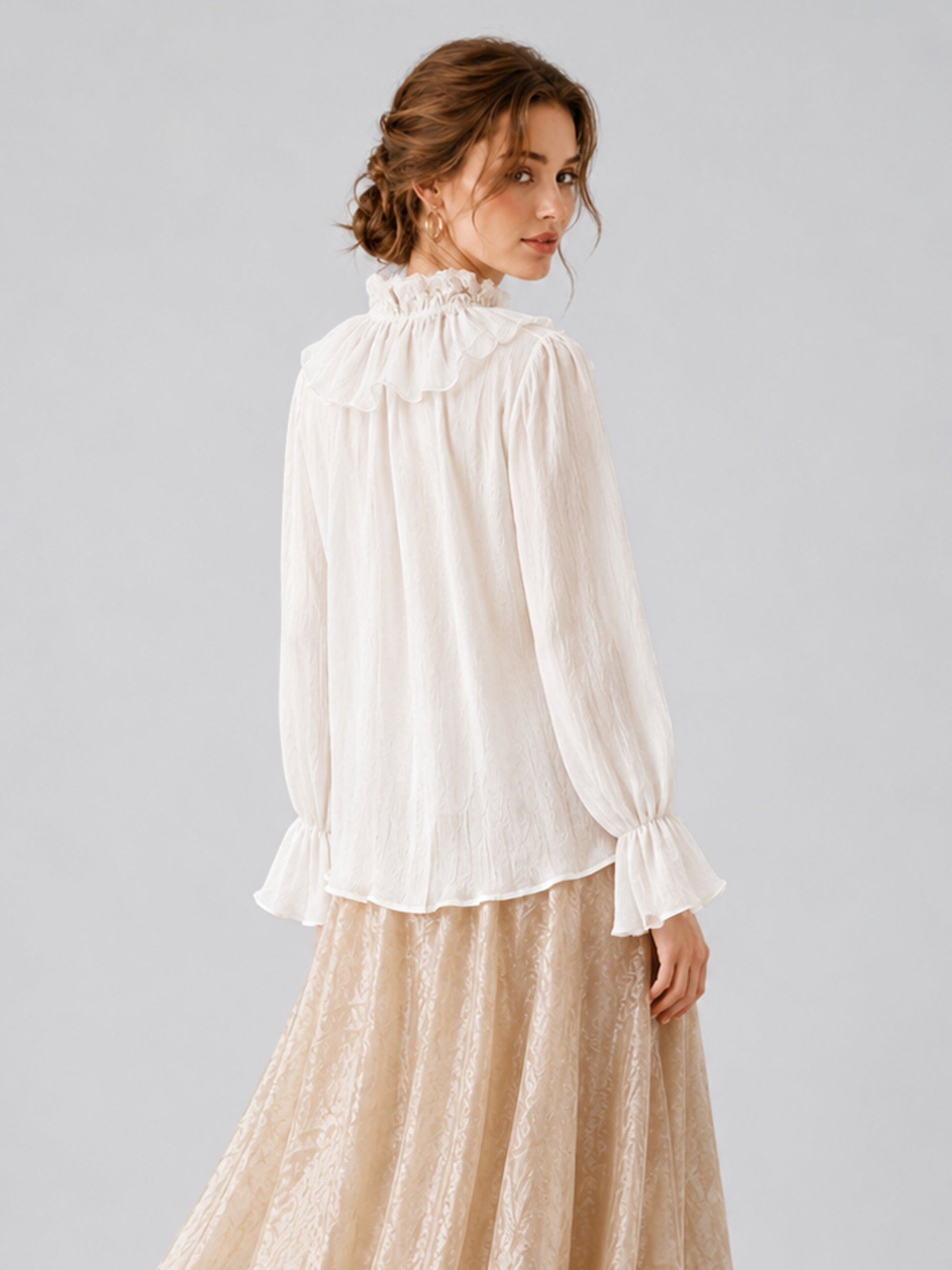A woman stands facing away, wearing the Social Queen Pearl Embellished Ruffle Collar Blouse with long sleeves and a beige lace skirt, her hair styled in loose waves against a plain gray background.