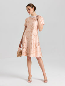 A woman wears the Social Queen Pearl Embellished Jacquard Dress, featuring a metallic rose motif and pearl neckline, holding a small purse against a plain light background.
