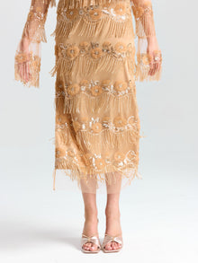 A person models the Social Queen Beaded Fringe Slit Midi Skirt, a knee-length, sheer gold design with sequin and bead embellishments, styled with open-toed heels against a plain background.