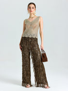 A woman faces forward wearing the Social Queen Open-Knit Metallic Sleeveless Top, paired with brown fringed pants and a brown handbag, accessorized with hoop earrings and heeled sandals.