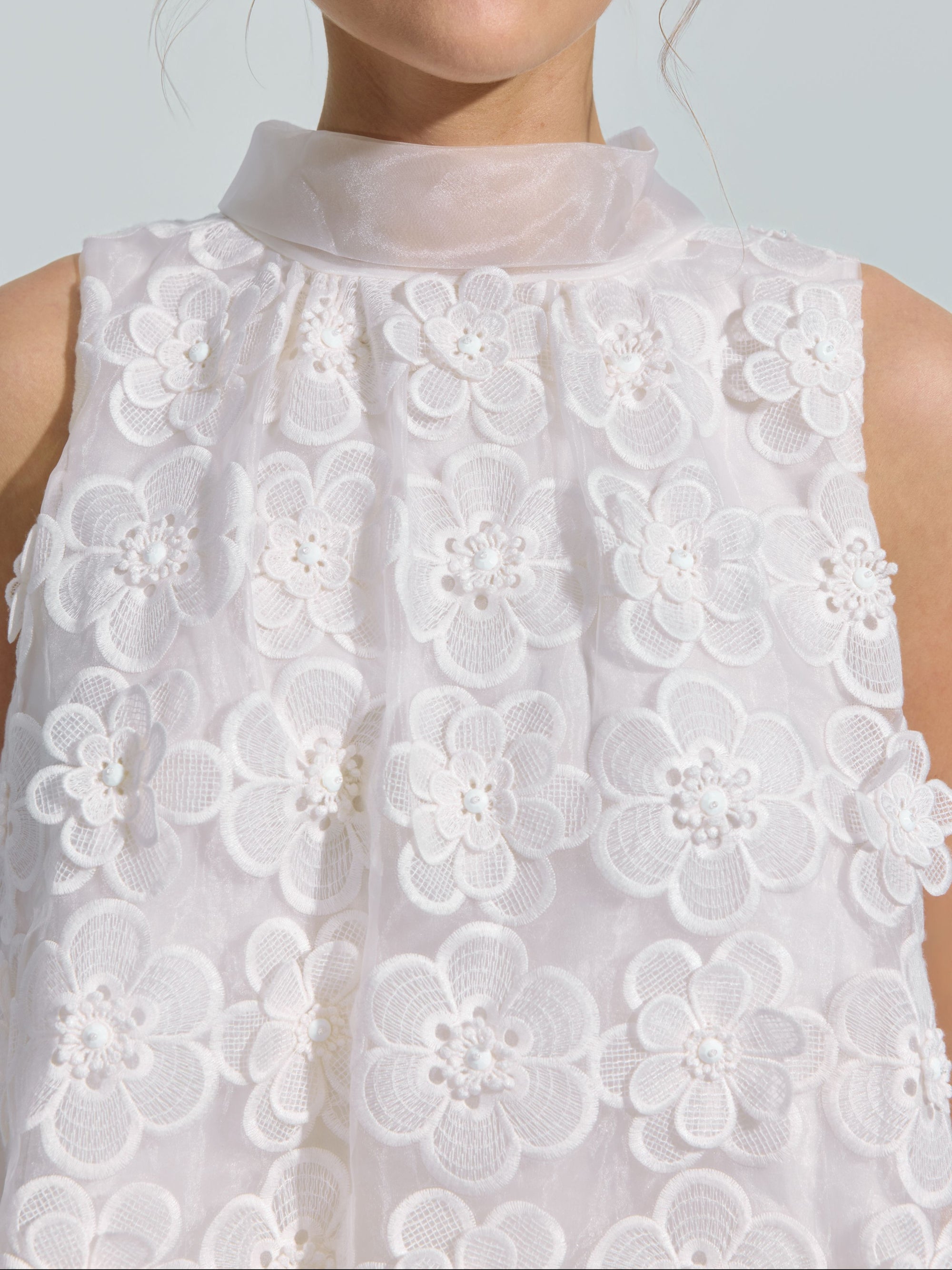 A person wearing the Social Queen 3D Floral Lace Appliqué Silk Top, featuring a sleeveless white design with sheer fabric, textured lace detailing, and delicate 3D floral embellishments.