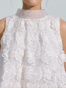 A person wearing the Social Queen 3D Floral Lace Appliqué Silk Top, featuring a sleeveless white design with sheer fabric, textured lace detailing, and delicate 3D floral embellishments.
