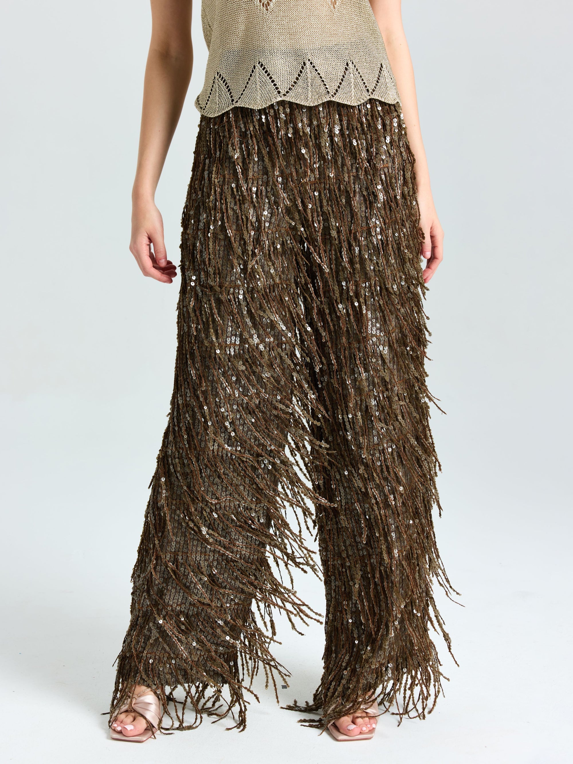A person wears Social Queen’s Sequin Fringe Wide-Leg Pants, styled with a beige knit top and open-toe sandals.