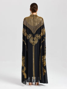 A person faces away in the Beaded Embroidered Cape Dress by Social Queen, a long black and gold chiffon piece featuring Persian-inspired embroidery—ideal for elegant evenings against a plain light background.