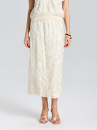 A person wearing the Social Queen Floral Embroidered Linen Midi Skirt with a light top, gold bracelet, and light pink open-toe shoes.