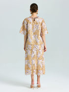 A woman faces away, wearing the Social Queen Floral Embroidered Lace Midi Skirt in beige and lavender with nude heels, set against a plain light background.