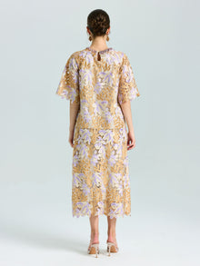 A woman faces away, wearing the Social Queen Floral Embroidered Lace Midi Skirt in beige and lavender with nude heels, set against a plain light background.