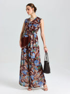 A woman models Social Queen’s Floral Print Wide-Leg Pants with a brown belt and fringe pouch, black woven handbag in hand—a relaxed, vacation-ready look set against a plain light background.