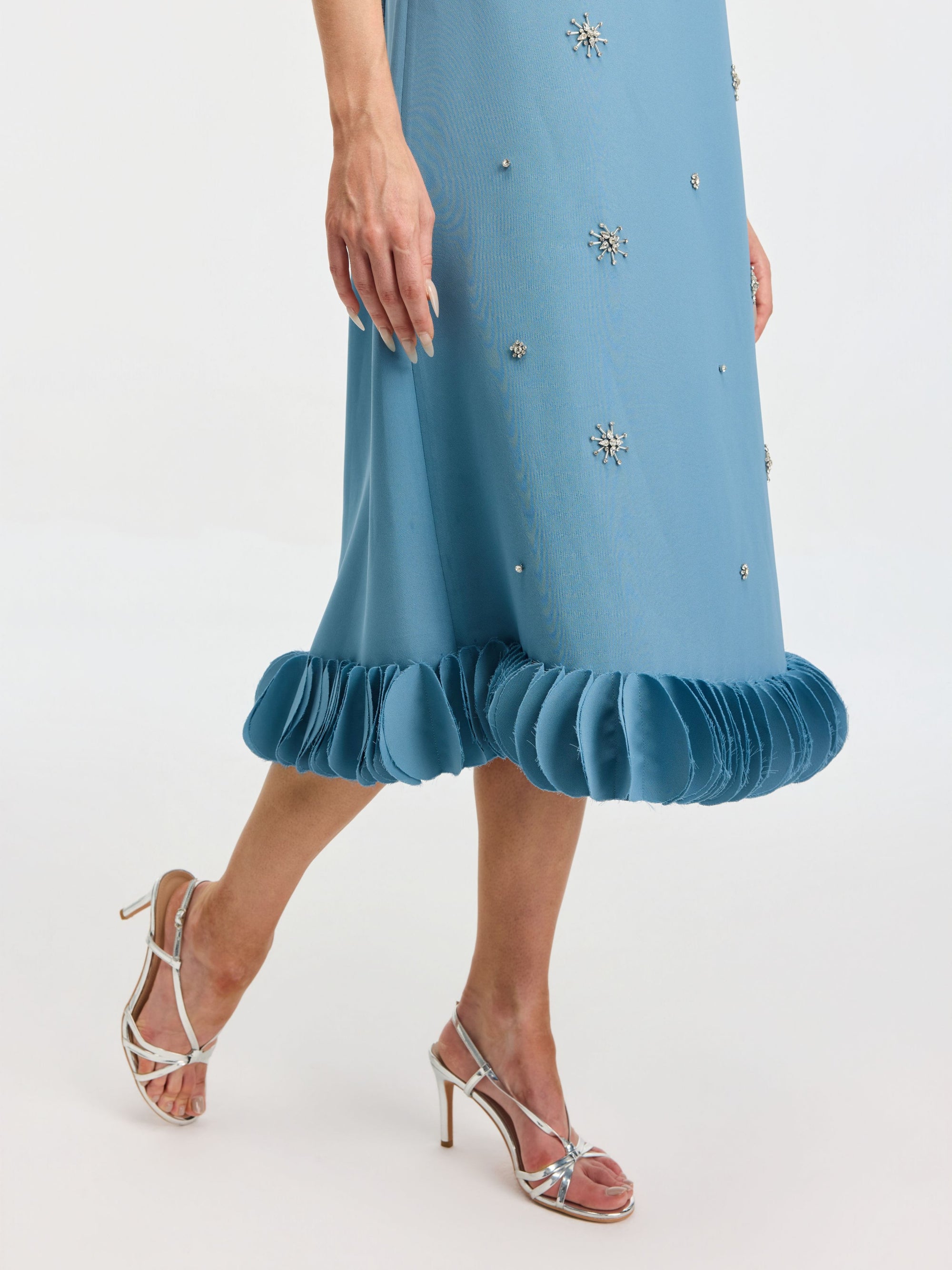 A person models the Social Queen Beaded Crystal Embellished Dress, featuring a shift silhouette, appliqué details, and ruffled hem, styled with silver high-heeled sandals against a white background.