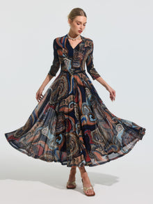 A woman poses with arms out and skirt fanned, wearing the Social Queen Paisley Print Knit Dress (Belt Included)—an ankle-length, long-sleeved A-line dress featuring a vibrant paisley pattern.