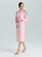 A woman wears the Social Queen Crystal Beaded Detail Midi Dress, featuring pink crepe fabric and crystal-embellished shoulders, styled with a metallic purse and heeled sandals—an elegant choice for evening events.