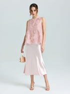 Woman wears the Social Queen Floral Bird Embroidered Silk Top—a sleeveless pink silk piece—paired with a shiny light pink midi skirt, open-toe heels, and a small pink handbag, posing against a plain light background.