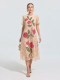 A woman wearing the Social Queen Hydrangea Embroidered Openwork Dress, a knee-length beige A-line with red and green floral lace, holds a small beige handbag and wears sandals against a plain background.