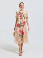 A woman wearing the Social Queen Hydrangea Embroidered Openwork Dress, a knee-length beige A-line with red and green floral lace, holds a small beige handbag and wears sandals against a plain background.