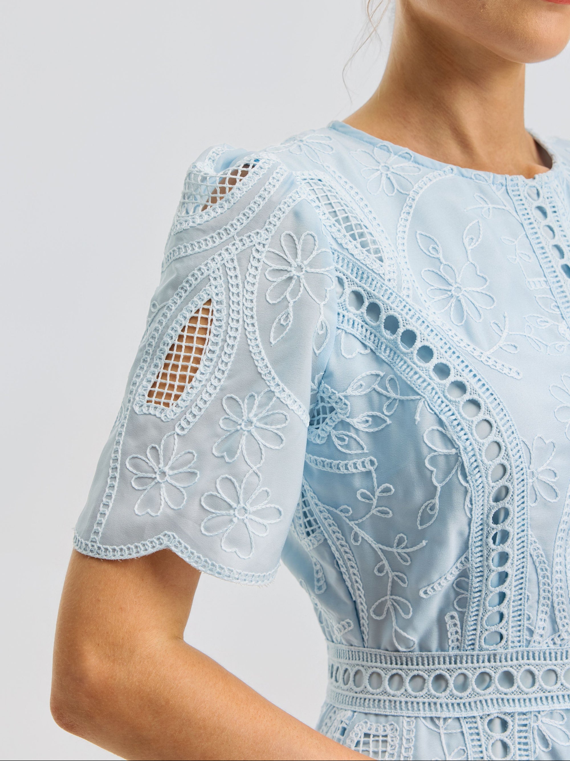 Close-up of a woman wearing the Floral Cutwork Embroidered Dress by Social Queen, crafted in a light blue silk-blend and adorned with floral embroidery, featuring intricate eyelet details and cutouts on the short sleeves.